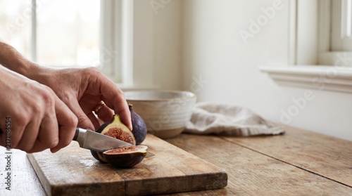 Hands slicing fresh fig on wooden cutting board in kitchen