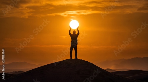 Silhouette of a person standing on a sand dune holding the sun with Dark figure man standing dune peak holding glowing orb
