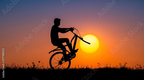 Silhouette of a man riding a bicycle against a bright sunset with cycling past glowing glowing orange sun