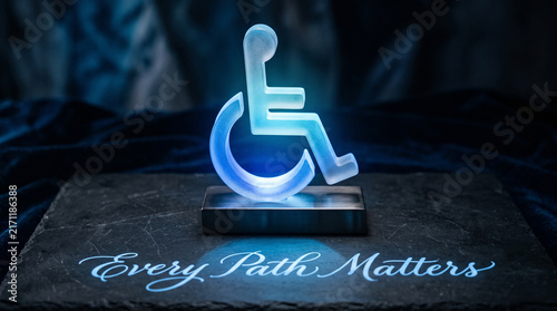 Illuminated frosted glass wheelchair accessibility symbol standing on a dark stone slab with engraved text with surface