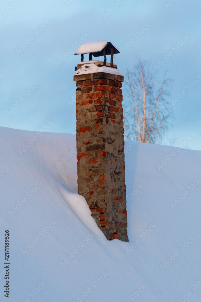 Fototapeta premium Snow-covered brick chimney stands tall against winter sky