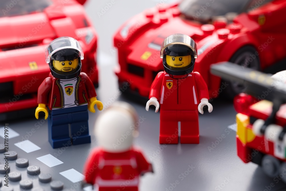 Fototapeta premium Tambov, Russian Federation - July 12, 2026 Lego Ferrari racing driver minifigures standing on a road baseplate with Ferrari sports cars in the background. Lego Speed Champions.