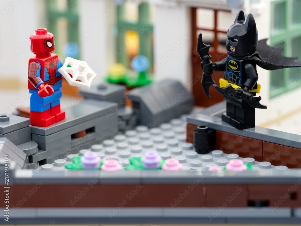 Fototapeta premium Tambov, Russian Federation - August 23, 2026 Lego Spider-Man holding a web piece and Batman wielding batarangs while standing opposite each other on a brick rooftop.