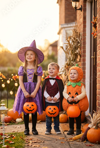 Three children in Halloween costumes holding pumpkins in autumn  