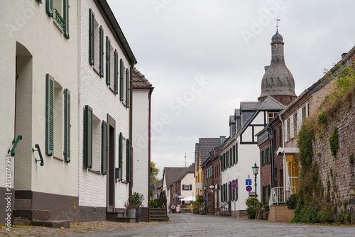 Canvas Print Historic houses line a narrow street leading toward a Juddeturm tower in Zons