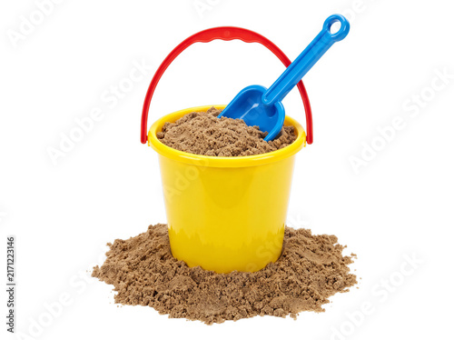 Colorful plastic beach bucket filled with sand and blue shovel, yellow toy pail with red handle, summer vacation sand toys on white background