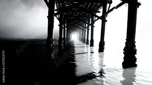Black and white shot of a pier in the fog with light at the end symbolizing hope and tranquility