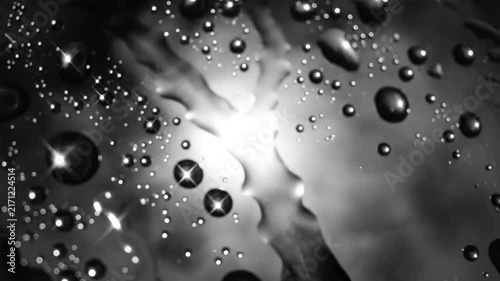 Black and white close up of water droplets illuminated with bright light reflecting on surface creating abstract pattern