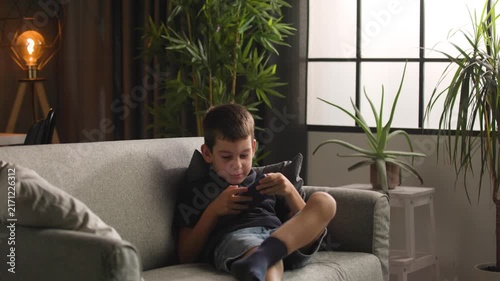 Young boy running to sofa sitting down to play game on smartphone