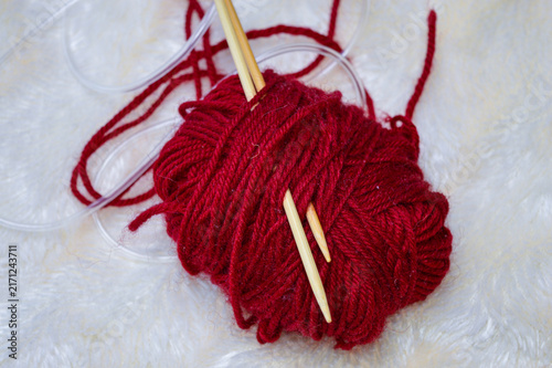 фотографія Ball of deep red yarn with wooden circular knitting needles inserted into it close-up