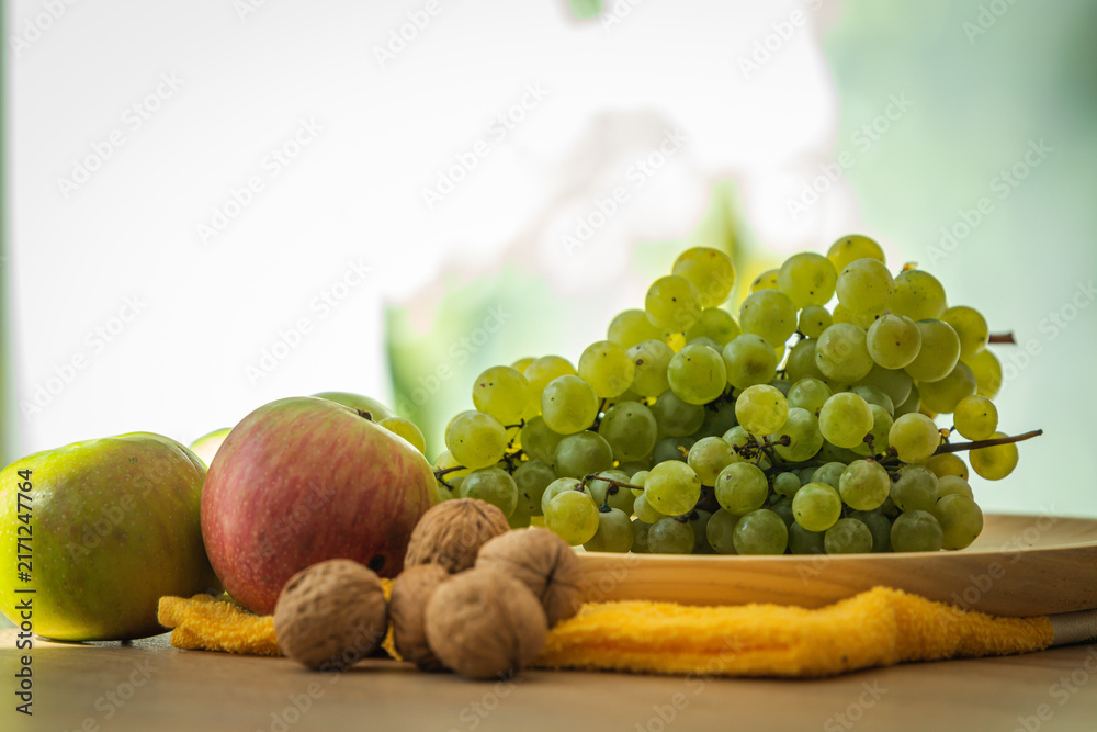 Naklejka premium Fresh green grapes, red and green apples, and walnuts arranged on a wooden tray — perfect for healthy eating, nutrition, and organic lifestyle concepts