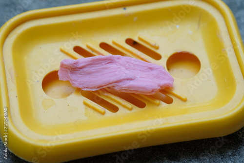 Quadro su tela Soap remnant in pink color resting on a yellow soap dish with drainage holes, sh