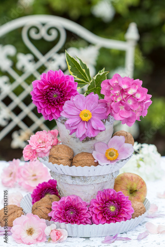 Etagere mit pink Herbstanemonen, Dahlien, Hortensienblüten, Rosen, Walnüssen und Äpfeln im Garten