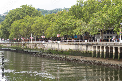 View of the riverside path with trees and buildings along the water