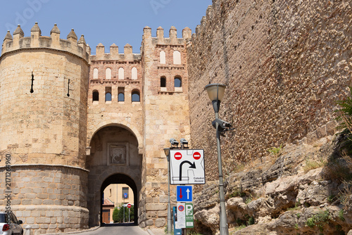 View of an old castle gate in a town with a stone wall nearby on a sunny day