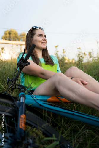 Obraz na płótnie Young woman with relaxed smile resting beside bicycle in open field, wearing bri