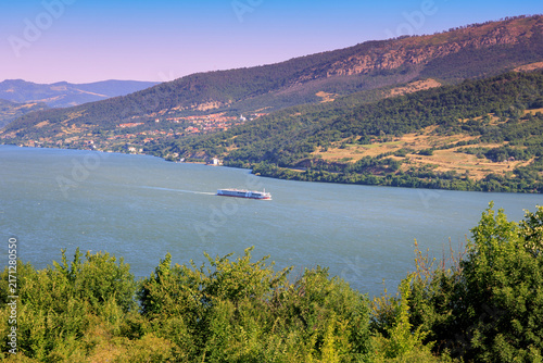 Cuadro en lienzo Bright summer light over the wide Danube River as a cruise ship glides through a green mountain gorge