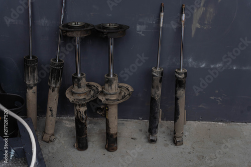 Fotografía Worn suspension struts and shock absorbers lean against painted wall, showing rust, grime, damaged boots on each unit