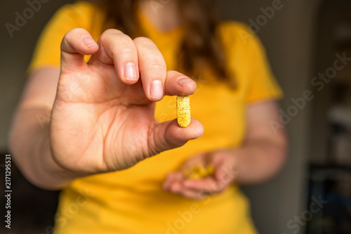 Cuadro en lienzo Close-up of a person presenting a yellow supplement tablet while holding additio