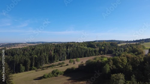 Aerial view of a bright rural landscape in sunny weather, featuring lush green vegetation, open countryside and winding roads surrounded by natural scenery.