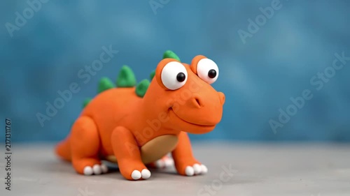 Cute Orange Clay Dinosaur Toy with Big Eyes on Blue Background.