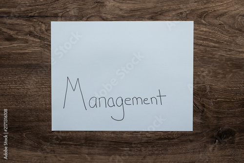 Flat lay background white sheet of paper with negative space and the word Management handwritten on lower portion on paper.