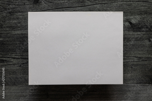 Birds eye view of blank sheet of paper against a dark grey wooden background.