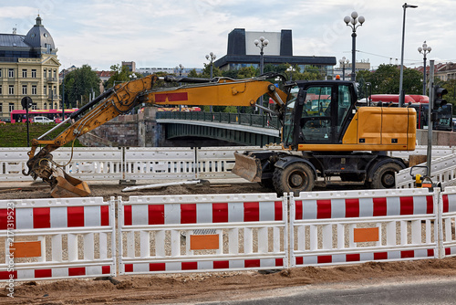 Canvas Print Yellow wheeled excavator on urban road construction site surrounded by safety barriers near bridge in city center