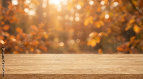 Rustic wooden table with blurred autumn leaves in warm golden sunlight