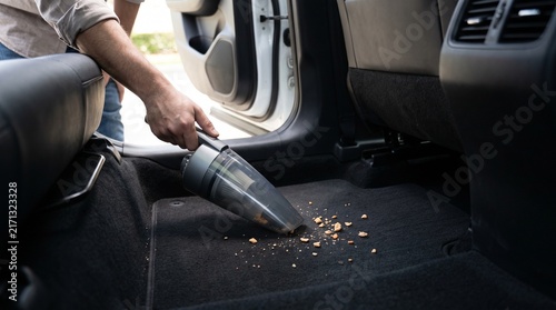Hand vacuuming food crumbs from car carpet floor mat