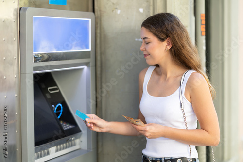 Obraz na płótnie Young girl in casual summer outfit stopping by ATM during walk in city to withdr