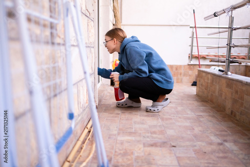 Teenage girl cleaning the lower frame of a balcony door.