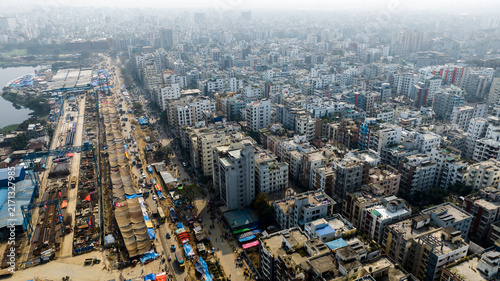 Aerial view of the dense urban landscape of Tongi with residential buildings, a construction site along the main road, and hazy sky in Tongi, Dhaka Division, Bangladesh.