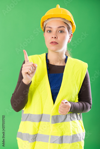 Portrait of young girl worker dressed in reflective vest and hard hat talking, actively gesturing, making prohibitive or