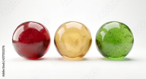 Three shiny glass marbles in red yellow and green colors on white background