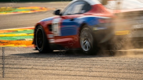 A thrilling display of speed and skill as high-performance vehicles compete fiercely on a sunlit race track, creating dynamic streaks of motion and kicked-up debris