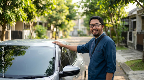 Smiling southeast-asian man standing beside his car on a sunny residential street