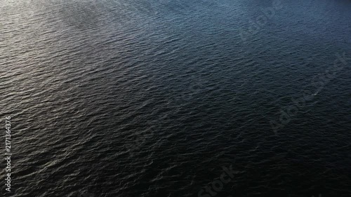 Waves move on the water surface as the sun sets. The light reflects on the water aerial view. It shows the beauty of the evening by the shore.