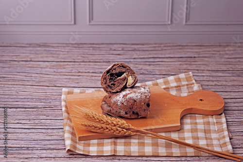 Sliced sourdough rests on a wooden board. Flour dusted loaf shows soft, chewy interior. Two wheat stalks add rustic charm. Checkered cloth beneath board enhances warmth. Ideal for food, bakery