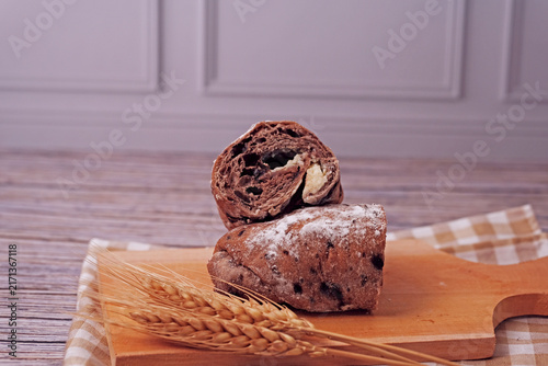 Sliced sourdough rests on a wooden board. Flour dusted loaf shows soft, chewy interior. Two wheat stalks add rustic charm. Checkered cloth beneath board enhances warmth. Ideal for food, bakery