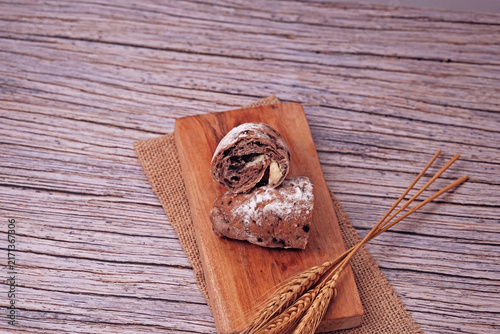 Sliced sourdough sits on wooden board. Sliced to reveal soft, creamy filling inside. Wheat stalks beside it hint at natural ingredients. Rustic wood surface adds warm, inviting tone