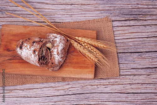 Sliced sourdough sits on wooden board. Sliced to reveal soft, creamy filling inside. Wheat stalks beside it hint at natural ingredients. Rustic wood surface adds warm, inviting tone