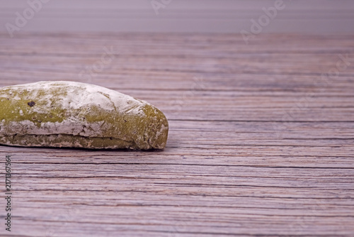 Fresh sourdough dusted lightly with flour rests on wooden surface. Subtle cracks mark its golden crust. Soft lighting enhances texture and warmth. Simplistic background draws focus to baked good