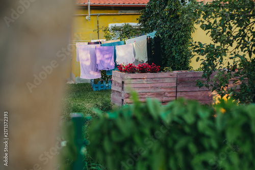 Laundry drying on clothesline in home backyard garden. Towels and clothes hanging outdoors near house with flowers. Domestic washing, rural lifestyle concept.