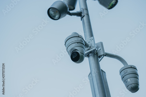 Security camera on pole against clear sky. CCTV video surveillance system monitoring city street. Urban safety, public protection and crime prevention technology concept.