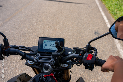 Rider's pov on motorcycle handlebar with digital display showing speed and gear, traveling down a road, feeling freedom and adventure on a journey