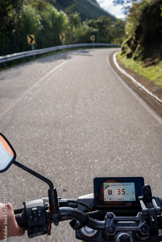 Person riding motorcycle on winding mountain road, enjoying journey and freedom with dashboard view, speedometer displaying speed, feeling adventure and exploring nature