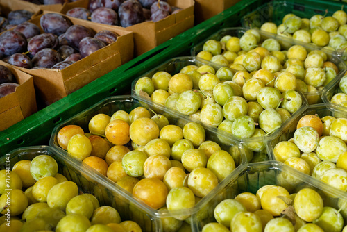 Bild auf Leinwand Fresh ripe yellow mirabelle plums in plastic punnets alongside purple plums displayed at a local market stand