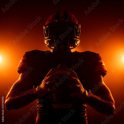 American football player holding ball with dramatic orange backlight, intense sports action and focus