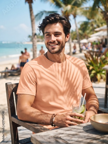 A man wearing a comfortable peach t-shirt, enjoying a refreshing drink on a sunny beach day with a tropical vibe